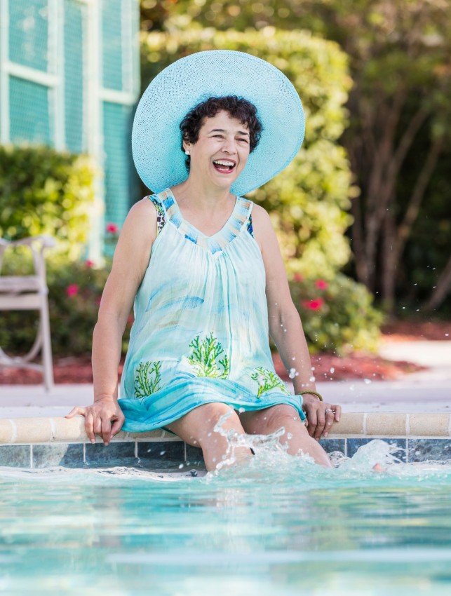 Happy woman splashing feet sitting beside pool