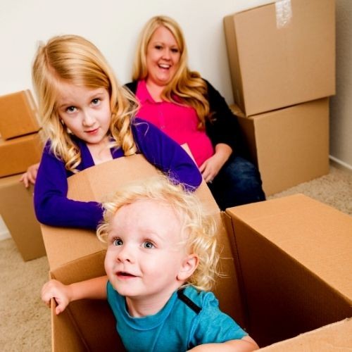 Baby in moving box with his big sister and mother behind him